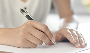 Person with a pen in hand, writing on a piece of paper.